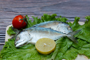 Mackerels with vegetable, lemon and tomato on wooden background.