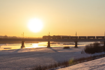 The train rushes along the railway bridge in the bright rays of the rising sun.