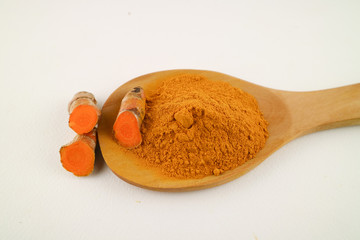 Turmeric powder in a spoon and turmeric root on a white background, used as a tonic for body and food ingredients.