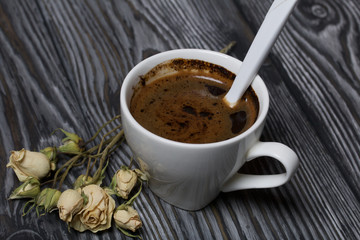 Coffee in a white cup. Nearby lies a flower of a dried beige rose. On brushed pine boards.