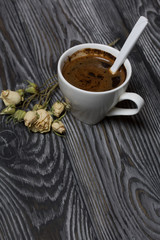 Coffee in a white cup. Nearby lies a flower of a dried beige rose. On brushed pine boards.