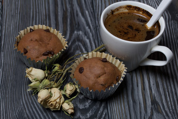 Coffee in a white cup. Nearby are muffins, and a dried rose of beige color. On brushed pine boards.