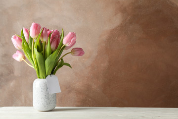 Vase with tulips on wooden table, space for text