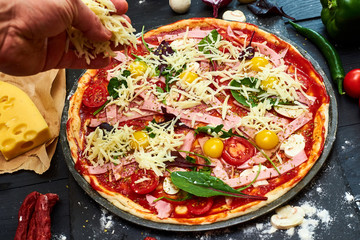 Raw pizza with mozzarella cheese, tomatoes, mushrooms, pepper, herbs on a dark wooden background. Cooking delicious italian pizza, add cheese.