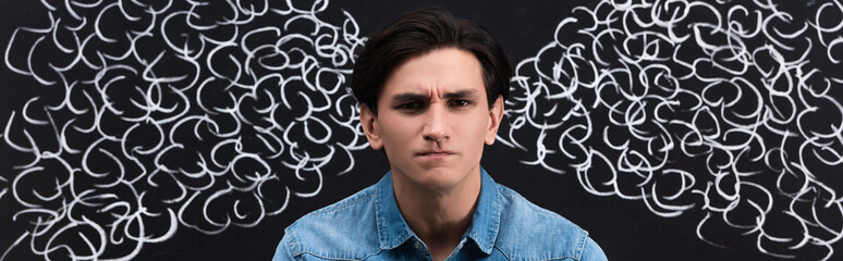 panoramic shot of irritated young man with steam drawing on blackboard behind