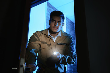 Professional security guard with flashlight checking dark room