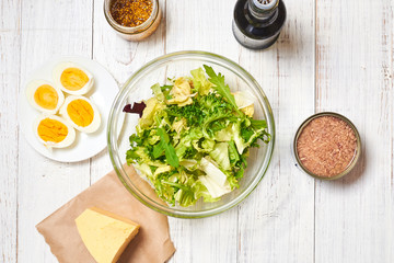 Making a salad of a mix of fresh vegetables and chicken eggs, tuna, mustard, cheese on a white wooden background. Healthy and wholesome organic food, diet, proper nutrition concept.