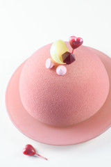 Contemporary Ruby Chocolate Dome Mousse Cake, covered with ruby velvet spray, decorated with meringue cookies, raspberry jelly, white chocolate shell and heart shape sauce capsule, on white background