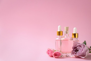 Bottles of essential oil and flowers on pink background. Space for text