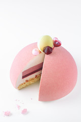 Contemporary Ruby Chocolate Dome Mousse Cake, covered with ruby velvet spray, decorated with meringue cookies, raspberry jelly, white chocolate shell and heart shape sauce capsule, on white background