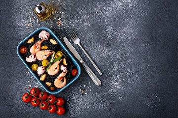 black pasta with seafood-shrimp, mussels, octopus, cherry tomatoes in blue plate on gray background