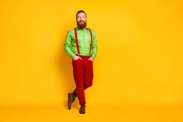 Fototapeta na wymiar Full length photo of attractive funky guy good mood looking side empty space cheerful wear green shirt red suspenders pants socks footwear isolated yellow color background