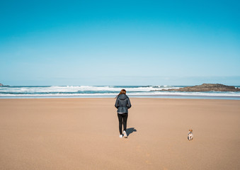 Woman walking on the beach sand with her dog and the sea waves in the background