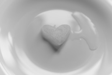 A snowy heart melts on a white plate. Heart shaped snow on a saucer. Ice in frosty weather. Melted water is collected in a small puddle. Wooden background. Love on valentine's day concept