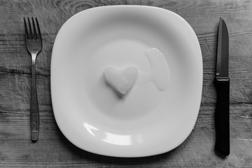 A snowy heart melts on a white plate. Heart shaped snow on a saucer. Ice in frosty weather. Melted water is collected in a small puddle. Wooden background. Love on valentine's day concept