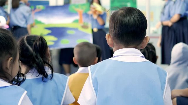  The small Asian children before kindergarten in white and light blue uniform  are sitting and watching fun and enjoyable story-telling activities.