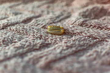 Gold modern earrings of large size, completely covered with small white transparent stones cubic Zirconia, creating artificial gold in a fashionable piece of jewelry on a velvet pink background
