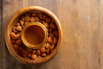 Apricot kernels in round bowl, glass jar with nut butter in center on wooden background. Food concept with copy space. Product for cardio vascular system, full of vitamims. Top view