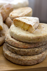 Several heads of cheese are stacked on top of each other for sale. Vertical photo