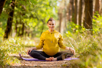 young pregnant woman doing yoga in the summer in the forest,Pregnant practices yoga outdoors. Prenatal Yoga and Fitness Future mom doing stretching exercises.