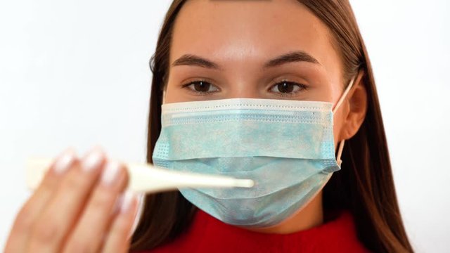 Girl in a medical mask looks at the thermometer in surprise
