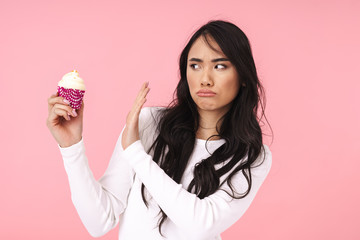 Image of young brunette asian woman gesturing no while holding cupcake