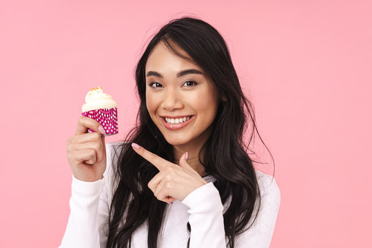 Image of young brunette asian woman smiling and holding cupcake