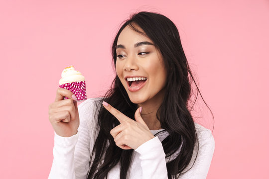 Image of young brunette asian woman smiling and holding cupcake