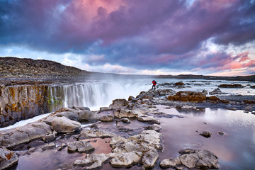 Photographer hiker with a travel backpack and tripod near Selfoss waterfall. Iceland, Jokulsa National Park, Fjollum river,  Europe. Travelling concept background. Golden Ring Of Iceland.