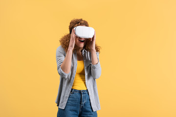 excited redhead girl using virtual reality headset, isolated on yellow