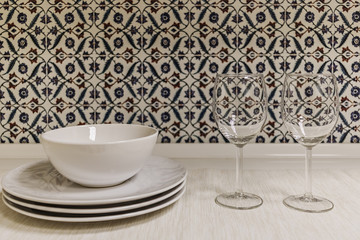 Clean plates and empty glass wine glasses prepared for dinner on the table, against the background of the kitchen