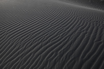 Black Icelandic Basalt Sand. Embossed sandy texture. Wavy background. Abstract pattern. Nature design. Reynisfjara beach with black volcanic sand. Stokksnes dunes. Reynisdrangar, Vik, Iceland Europe