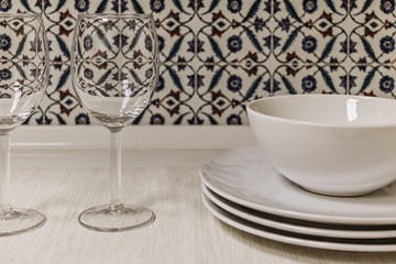 Clean plates and empty glass wine glasses prepared for dinner on the table, against the background of the kitchen