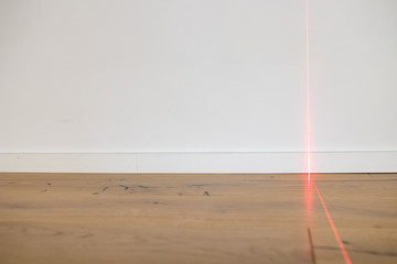 Laser meter on white wall and parquet in new apartment. Precision measurements on building renovation sites for architects and carpenters and bricklayers. Red laser beam on wall and copyspace