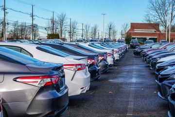 View of the back of a row of various colored new cars in a parking lot