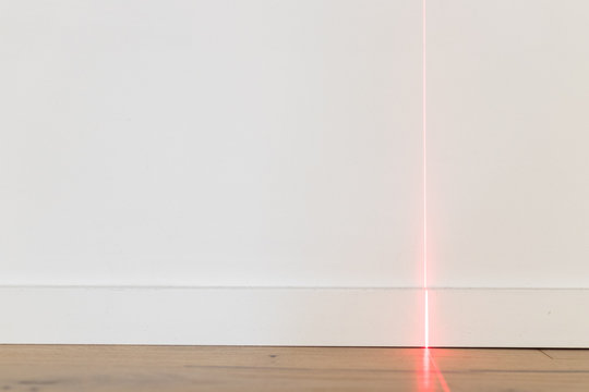 Laser meter on white wall and parquet in new apartment. Precision measurements on building renovation sites for architects and carpenters and bricklayers. Red laser beam on wall and copyspace
