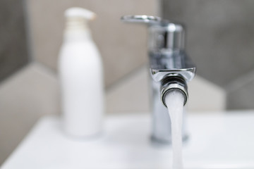 water flowing from a tap in a home bathroom. bathroom supplies with flowing water and blurred background