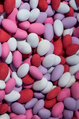 A bunch of colorful chocolate dragees. Almond covered with chocolate and multicolored glaze. Red pink and purple sweets. Candy shop. Candy background. Vertical photo.