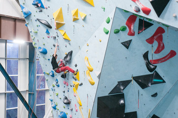 Man climbing in a gym. Climber on a wall. Climbing with rope. Colorful volumes and holds. Lead.