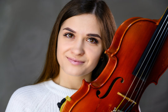 Concept musician violinist. Portrait of a pretty brunette girl in a white sweater playing the violin on a gray background
