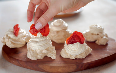 the process of creating Pavlova dessert, decorating the meringue with strawberries