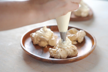 the process of creating Pavlova dessert, decorating the meringue with cream from the culinary bag