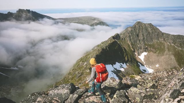 Hiker woman traveling in mountains girl with red backpack adventure hiking healthy lifestyle happy raised hands summer vacations activity trekking in Norway over clouds