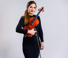 Portrait of a pretty brunette musician girl with a smile in a black dress on a white background holds a violin in her hands