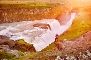 Gullfoss waterfall on the Hvíta river, a popular tourist attraction and part of the Golden Circle Tourist Route in Southwest Iceland. Man tourist in red jacket looks at the flow of falling water.