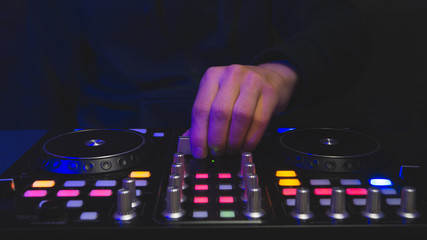 Obraz premium DJ plays music. sound mixer controller with knobs and sliders. hands on the mixing deck and turntables at dark with illuminated controls