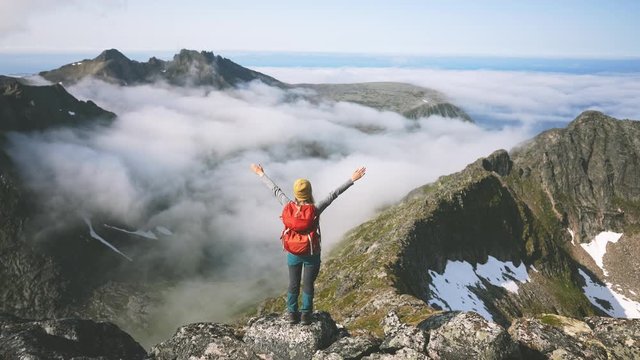 Woman with backpack hiking in mountains adventure travel vacations healthy lifestyle girl happy raised hands on mountain top over clouds summer activity exploring Norway