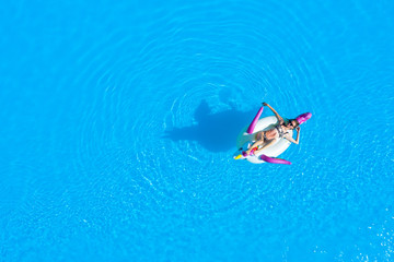 Top view of the pool with a girl in a swimsuit on an inflatable circle. Relaxing and tanning in the summer.