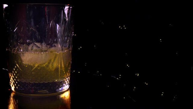 Close-up. Side VIew of Pouring Glass of Whiskey. Pouring of scotch whiskey or cognac into glasses with ice cubes on dark background