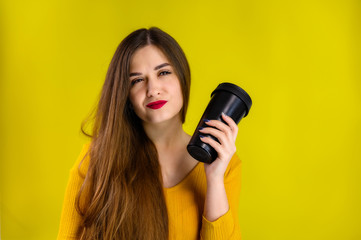 Obraz premium nice brunette girl with long hair with a smile with a cup of coffee in a yellow sweater is happy on a yellow background smiling and showing positive emotions